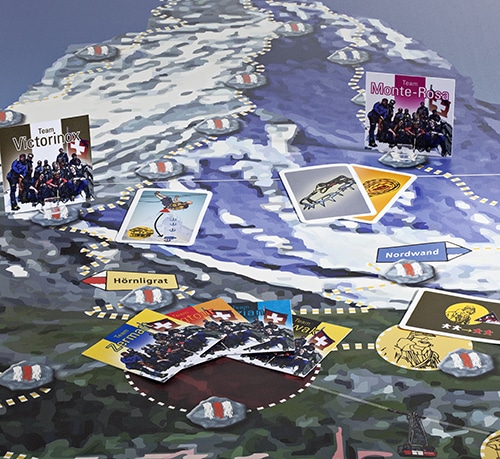 Ein Spielbrett mit Matterhorn: Kollaborierende Teams als Bergsteiger mit Ausrüstungskarten auf den Wanderwegen.