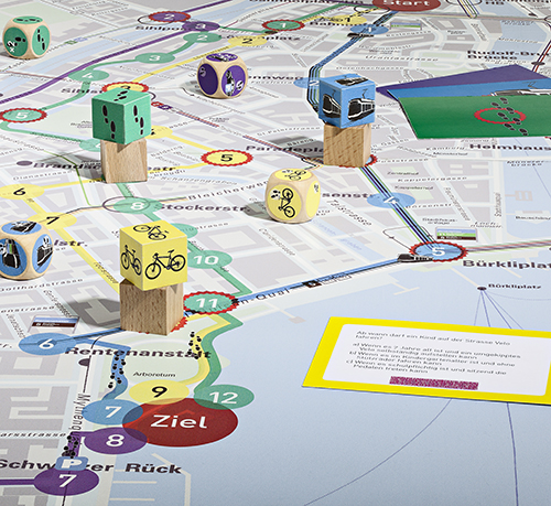 Eine Karte von Zürich, auf der verschiedene Verkehrsmittel dargestellt sind, mit Holzfiguren und Würfeln auf einem lebendigen Spielpfad und einer Karte mit einer Frage zur städtischen Mobilität, die den pädagogischen Fokus des Spiels auf nachhaltigen Verkehr betont.